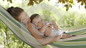 Smiling happy mother hugs and cuddle her little baby son, relaxing  lying together in the hammock. Child plays with pacifier, in