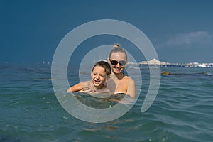 Smiling happy mother and son playing on the wave in the sea in the daytime. Happy family relaxing by the sea. Summer, spring and w