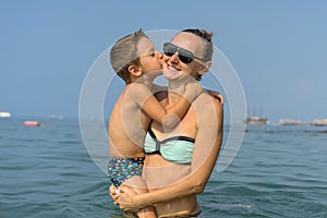 Smiling happy mother and son playing on the wave in the sea in the daytime. Happy family relaxing by the sea. Summer, spring and w