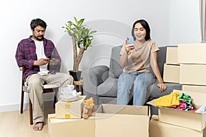 Smiling happy moving to a new house. Asian couple relaxing with smartphone at home, loving man and woman sitting on couch together