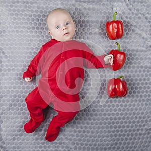 Smiling happy newborn infant three month baby in the red clothes with three peppers to indicate age