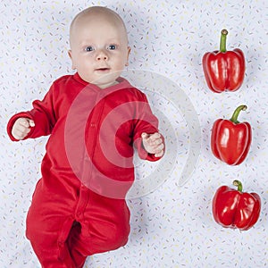 Smiling happy newborn infant three month baby in the red clothes with three peppers to indicate age