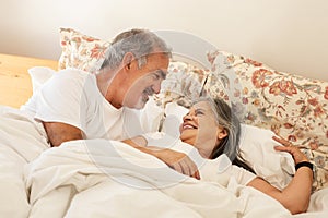 Smiling happy old caucasian husband wakes up wife in bed, enjoy good morning together in bedroom