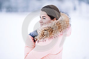 Smiling happy pretty woman in warm winter jacket outdoors enjoys winter journey, weared gloves and hood, a lot of snow