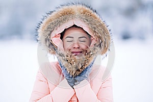 Smiling happy pretty woman in warm winter jacket outdoors enjoys winter journey, weared gloves and hood, a lot of snow