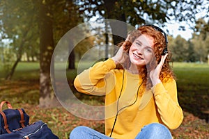 Smiling happy red hair student girl in headphones outside in autumn park