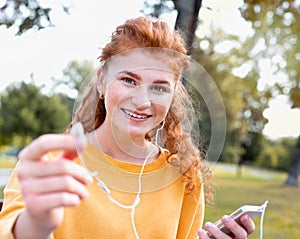 Smiling happy red hair student girl in headphones outside in autumn park