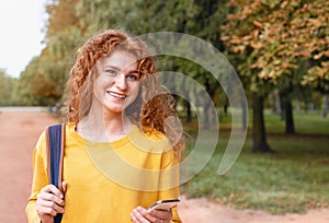 Smiling happy red hair student girl outside in autumn park
