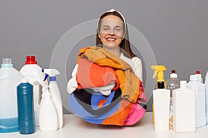 Smiling happy satified woman posing at workplace with cleaning detergents isolated over gray background doing laundry being happy