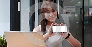 Smiling happy woman in casual showing blank smartphone screen while looking at the camera isolated over white background. Using