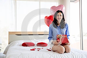 Smiling happy woman in love with gift box and rose in bedroom,Valentine's Day concept