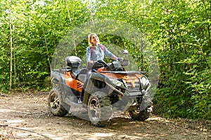 Smiling happy woman riding quad bike on a sunny day, against blue sky. Low angle shot. Freedom, happiness, nature