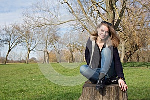 Smiling happy woman sitting on a tree stump