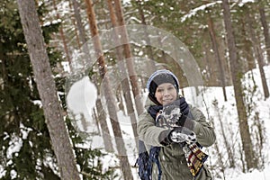Smiling, happy woman throws a snowball in the winter forest.