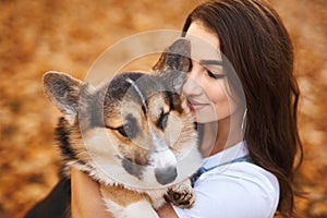 Smiling happy woman together with Welsh Corgi Pembroke dog in a park outdoors. Young female owner huging pet in park at