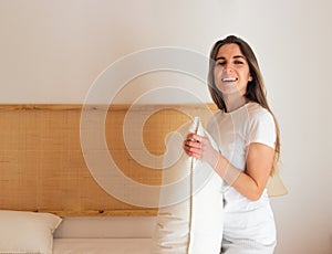 Smiling and happy young beautiful woman making the bed as home work on a boho and chic modern bedroom