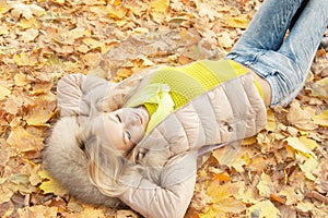 Smiling happy young blonde woman laying in autumn leaves, top view, healthy lifestyle concept
