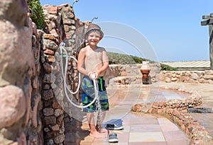 Smiling happy young boy rinsing off with a hose