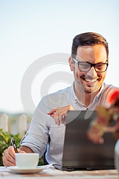 Smiling happy young businessman working in an outdoor restaurant, preparing for important meeting