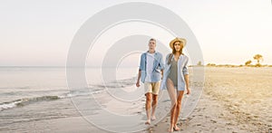 Smiling happy young couple, man and woman, wearing a blue shirt, holding hands, looking at each other, walking together