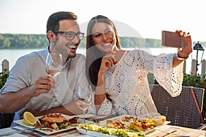 Smiling happy young couple posing for a selfie, eating dinner in a riverside restaurant
