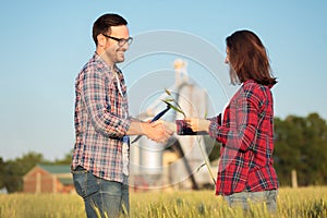 Smiling happy young male and female farmers or agronomists shaking hands in a wheat field. Inspecting crops before the harvest