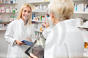 Smiling happy young and mature female pharmacists working behind the counter in a pharmacy