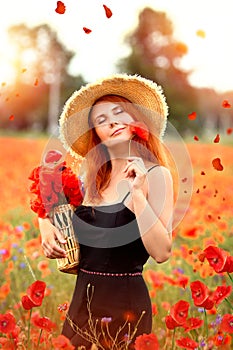 Smiling and happy young red-haired  woman in a black dress and a hat holding red poppies near the face. Beautiful poppy field at