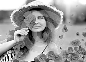 Smiling and happy young red-haired  woman in a black dress and a hat holding red poppies near the face. Beautiful poppy field at