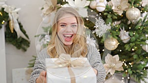 Smiling and happy young woman with christmas present box near christmas tree.