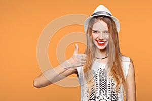 Smiling happy young woman showing thumbs up, isolated on orange background