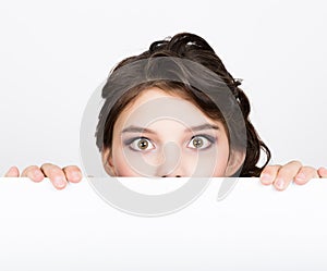 Smiling happy young woman standing behind and leaning on a white blank billboard or placard, expresses different