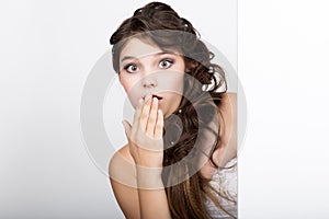 Smiling happy young woman standing behind and leaning on a white blank billboard or placard, expresses different