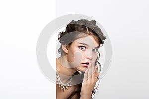 Smiling happy young woman standing behind and leaning on a white blank billboard or placard, expresses different