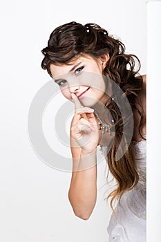 Smiling happy young woman standing behind and leaning on a white blank billboard or placard, expresses different