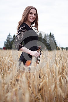 Smiling happy young woman violinist in a wheat field