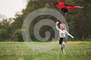 Smiling and having fun. Happy girl in casual clothes running with kite in the field. Beautiful nature