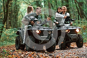Smiling and having fun. Two couples on a quad bike in the forest during the day