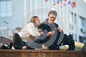 Smiling, having fun. Two young students are sitting outdoors against university