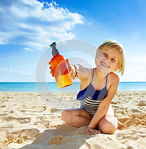 Smiling healthy child in swimwear on seacoast showing lotion