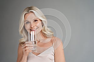 Smiling healthy thirsty fit mid aged 50s woman holding glass drinking water.