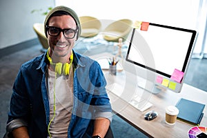 Smiling hipster businessman posing for camera while sitting at desk