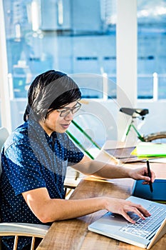 Smiling hipster businessman using laptop and graphic tablet