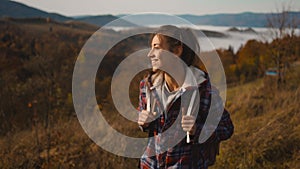 smiling hipster millennial young woman walks on top of mountain pass at morning, looking ahead, enjoying beautiful view