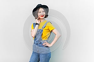 Smiling hipster woman in overalls, T-shirt and hat, looking away, dreaming for something pleasant.