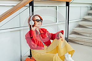 Smiling hipster young woman in bright clothes, sunglasses with backpack bag and wireless headphones listening to music