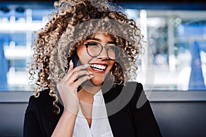 Smiling hispanic afro business woman wearing eye glasses in cafe using laptop and mobile phone