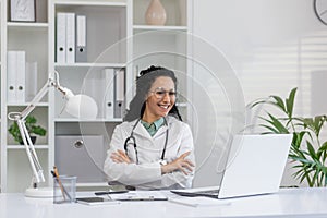Smiling Hispanic female doctor in clinic office with laptop