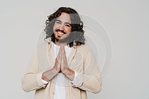 Smiling hispanic man doing pray gesture with folded hands while standing isolated