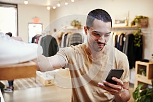 Smiling Hispanic man using smartphone in a clothes shop